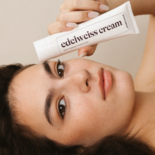 Model houdt Prescription Skincare Edelweiss Cream tube vast tegen haar wang